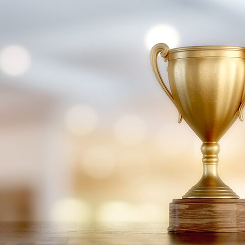 Gold trophy on right hand side of image. Soft, blurred office background in white.