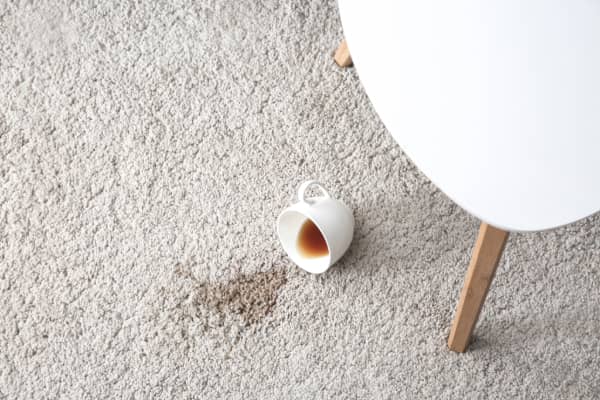 A coffee cup spilled on the carpet, leaving a stain beside a white chair.